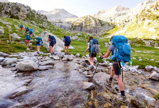 Travelers walking in a line over a stream, all with backpacks