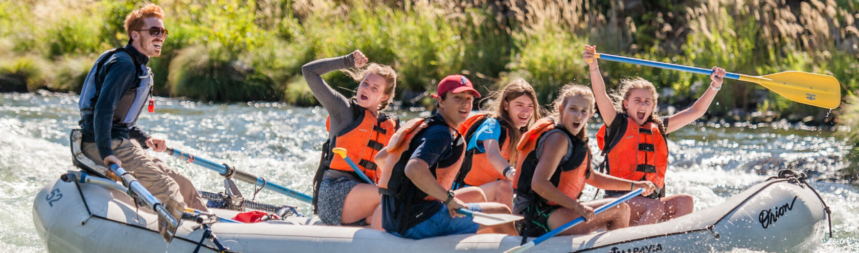 group of students on a araft laughing and celebrating passing through whitewater rapids