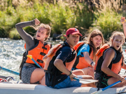 group of students on a araft laughing and celebrating passing through whitewater rapids