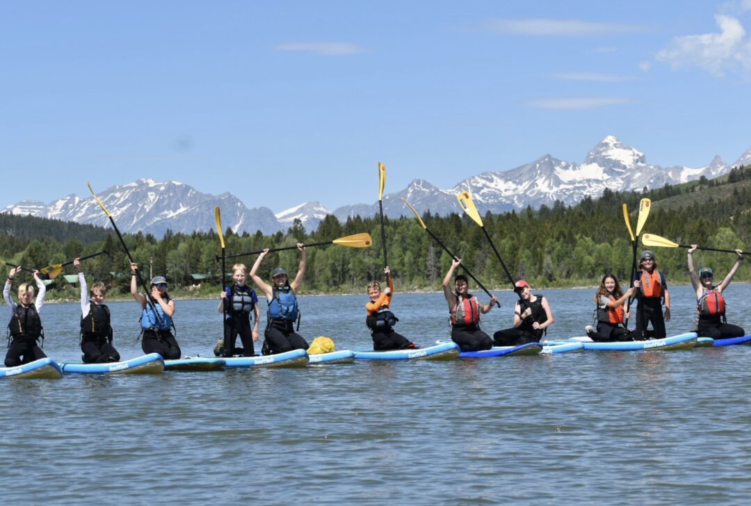 group paddle boarding in front of the Tetons raising their paddles