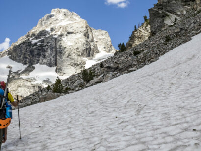 backpackers hiking through a snowfield toward Grand Teton