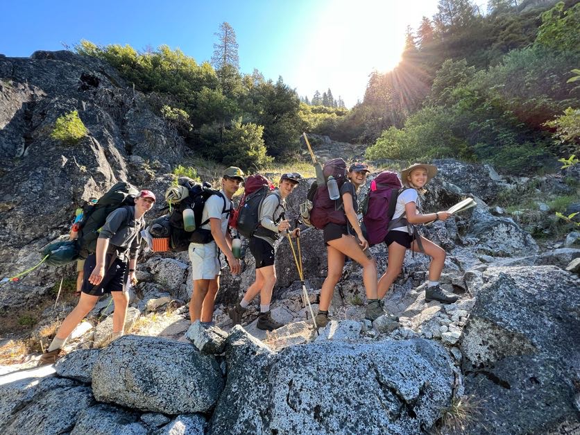 a group backpacks on a sunny, rocky trail