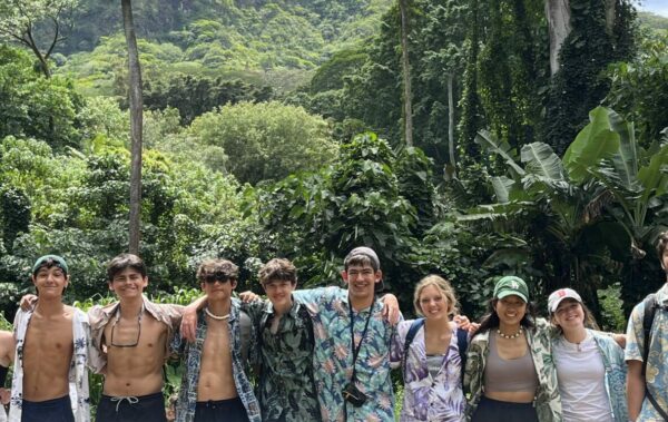 Group of student in hawaiian shirts in front of green plants and trees of hawaii