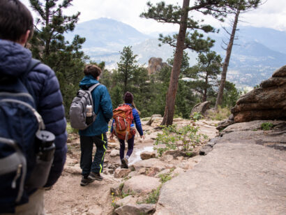 three people hiking through rocking mountain national park overlooking the town and landscape of Estes Park