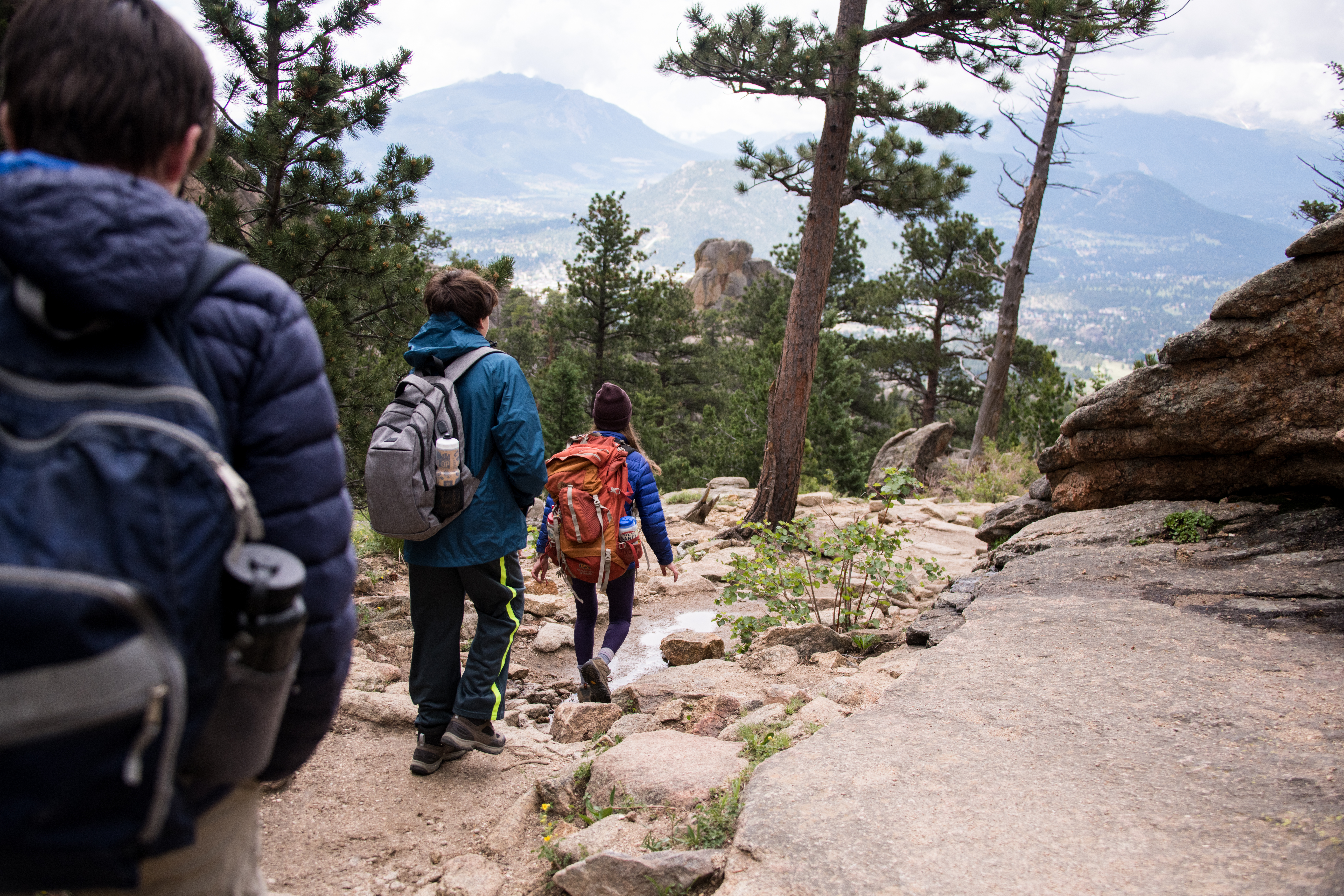three people hiking through rocking mountain national park overlooking the town and landscape of Estes Park