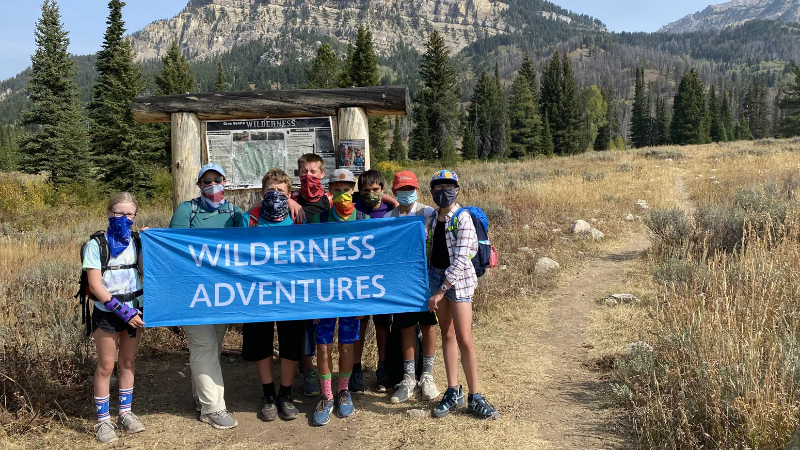 Travel group wearing masks holding a Wilderness Adventures sign