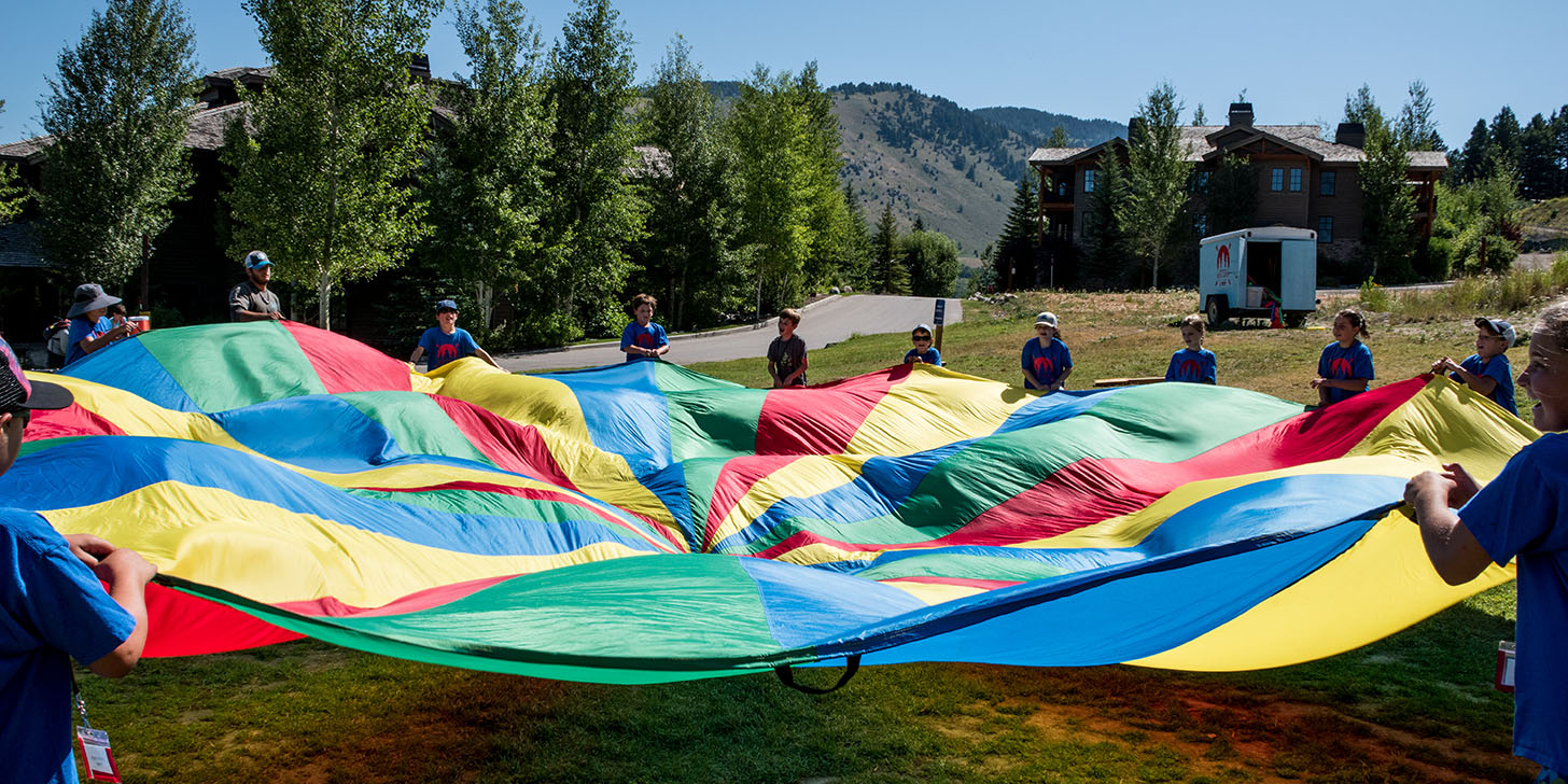 day campers playing outside with colorful parachute
