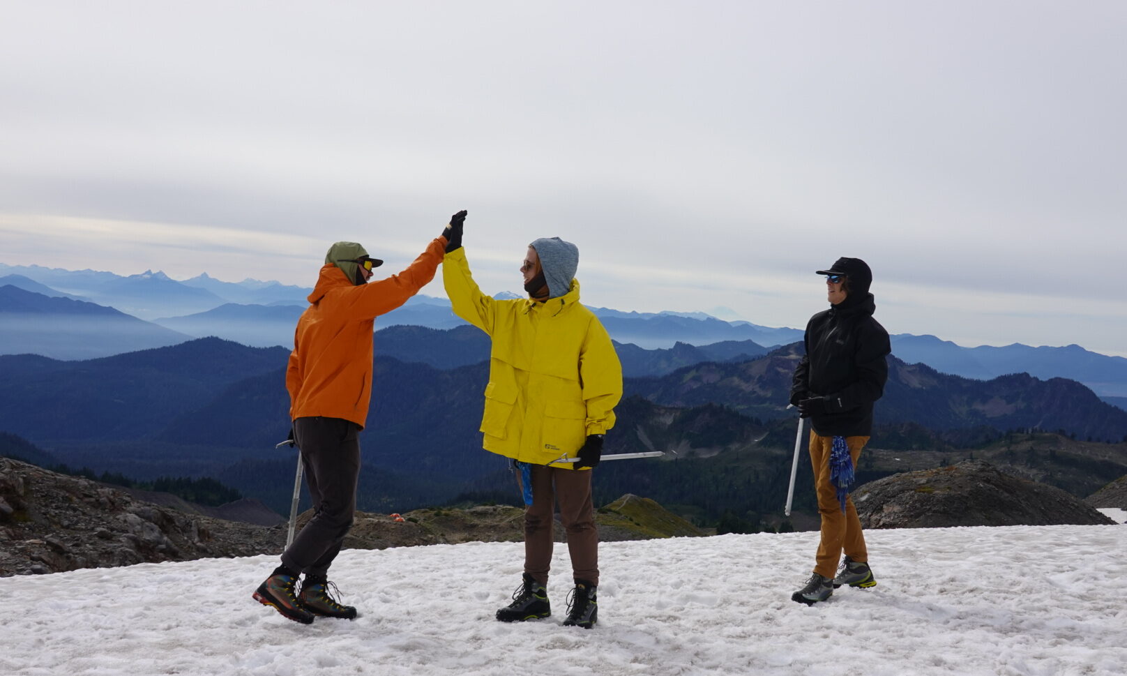 two people high fiving on top of a mountain with ice axes, and another person next to them