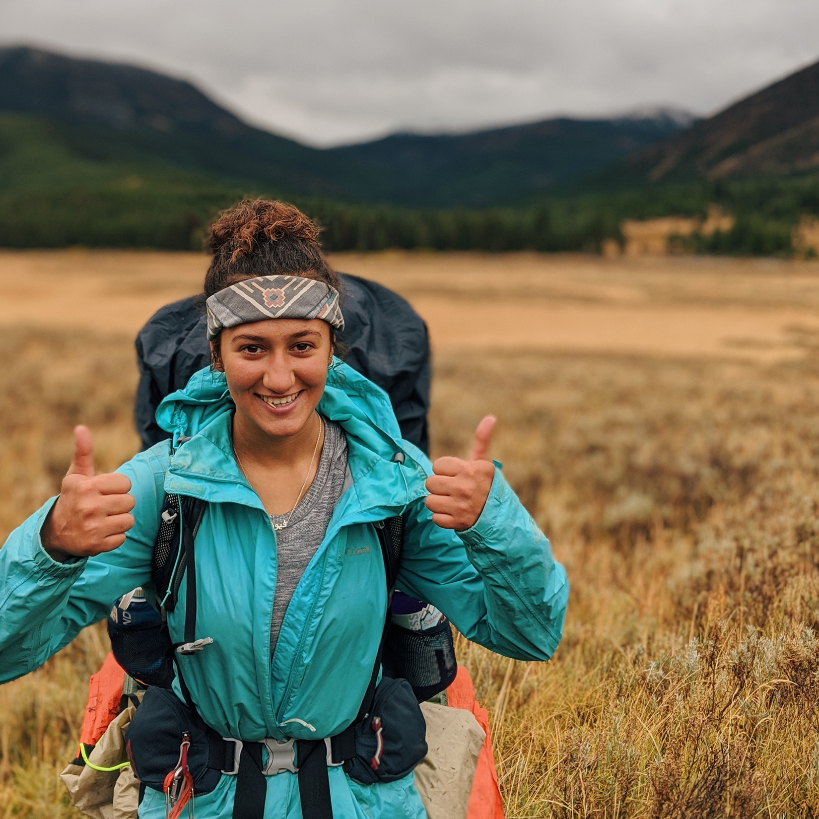 Woman with two thumbs up and backpacking gear on.
