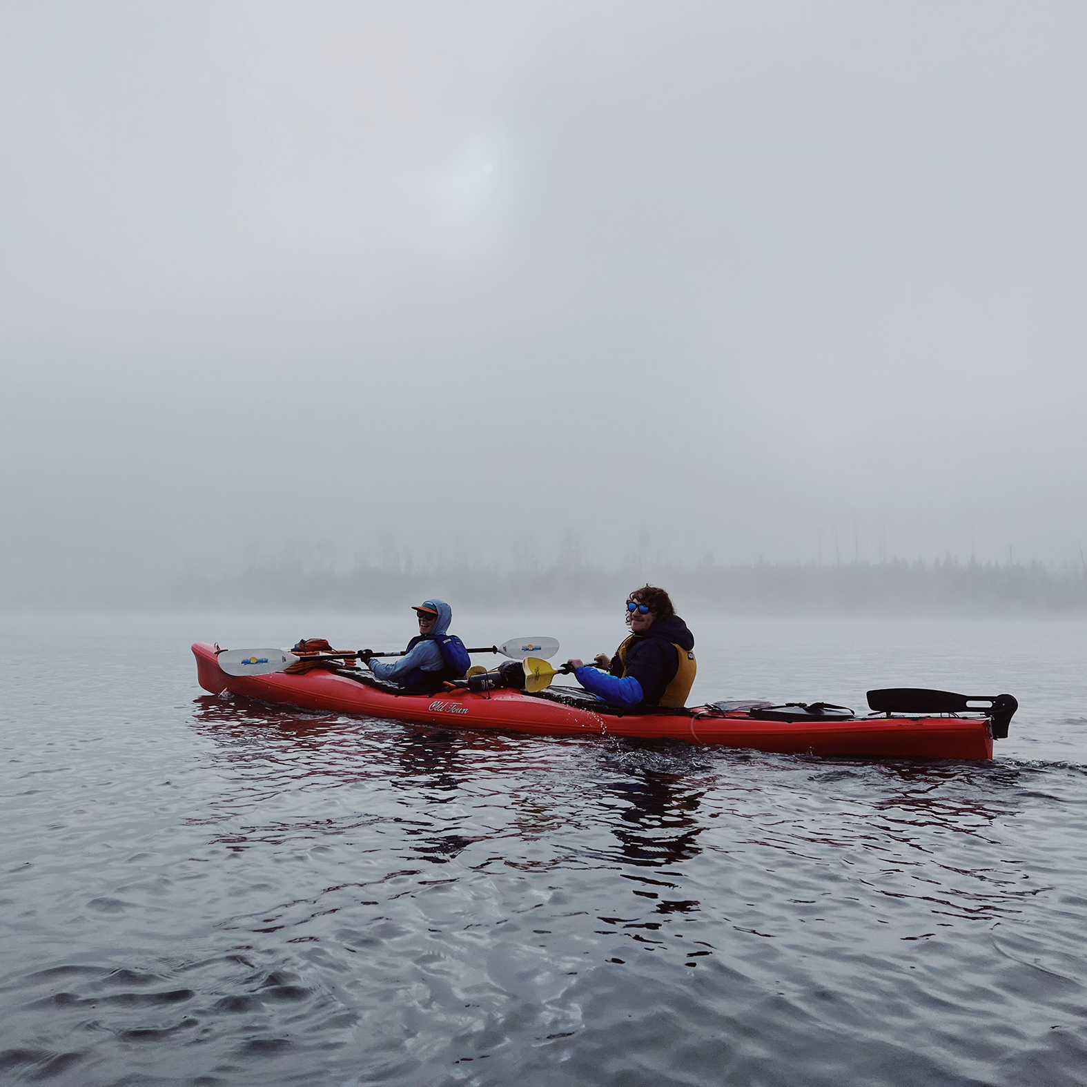Two people in a kayak paddling through fog.