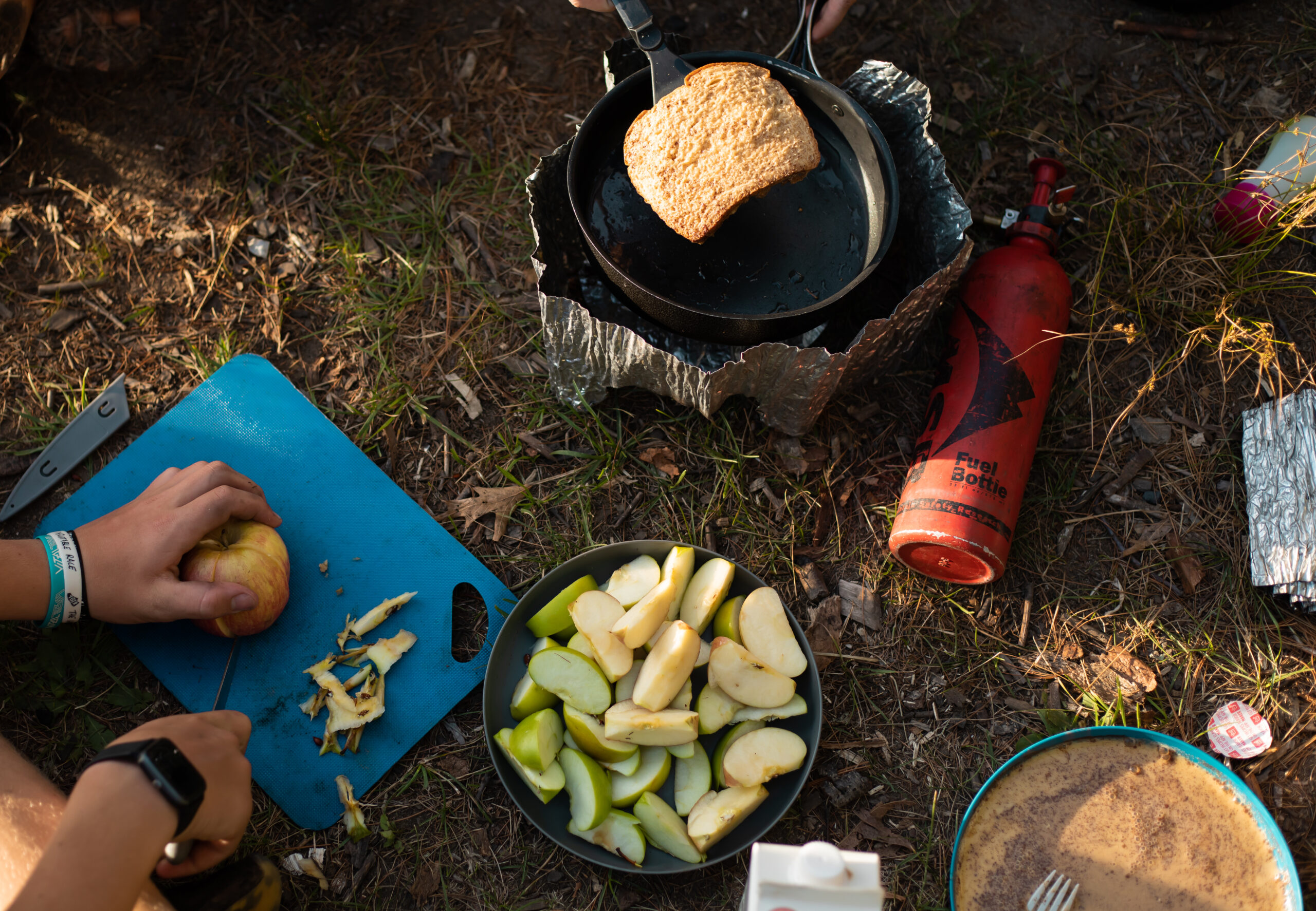 camping food preparation, cutting board with apples, and a backcountry stove flipping bread