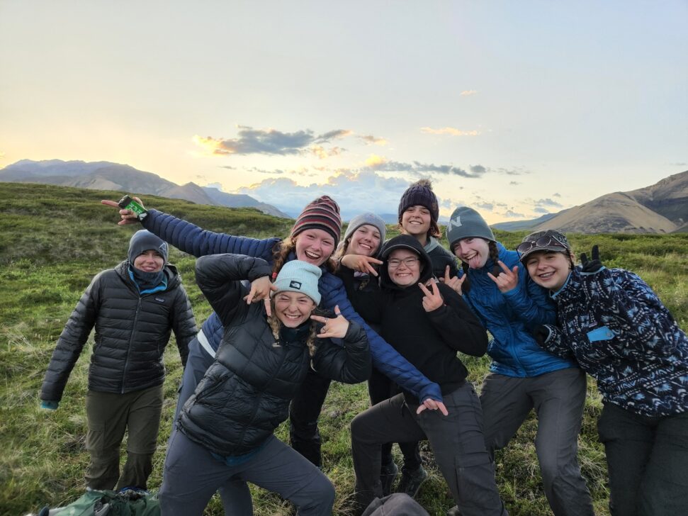 a group of teens smiling infront of an alaskan sunset