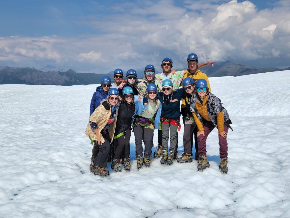 a group poses on a glacier in hawaiian shirts and ice climbing gear