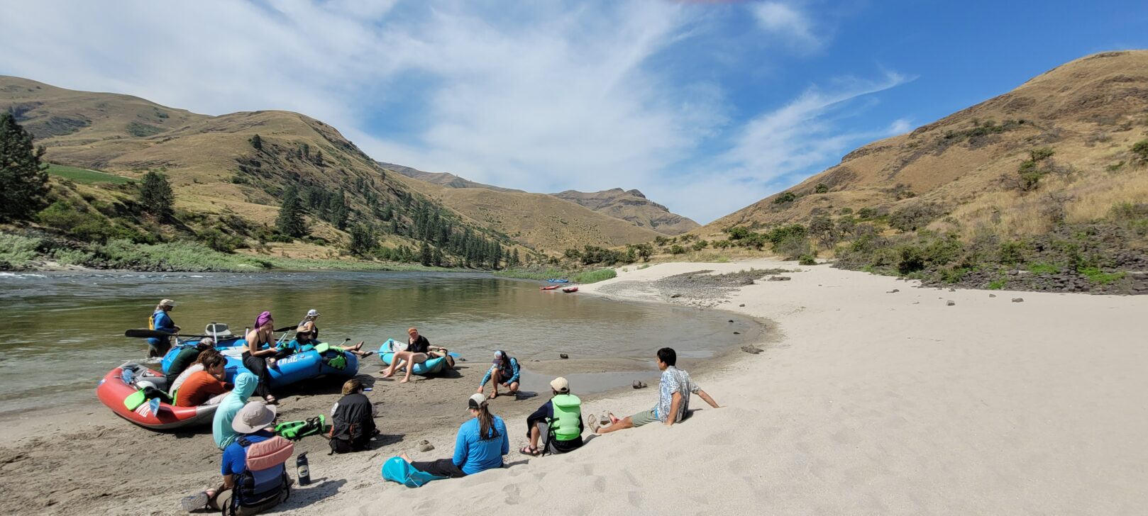 students resting on the shores of a river while rafting
