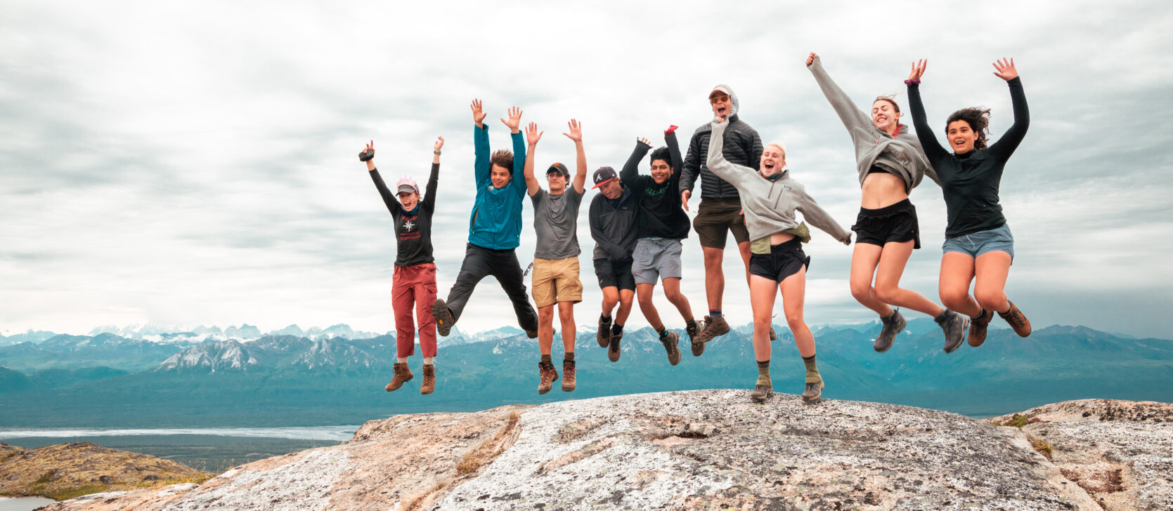 group jumping on a rock with mountains behind