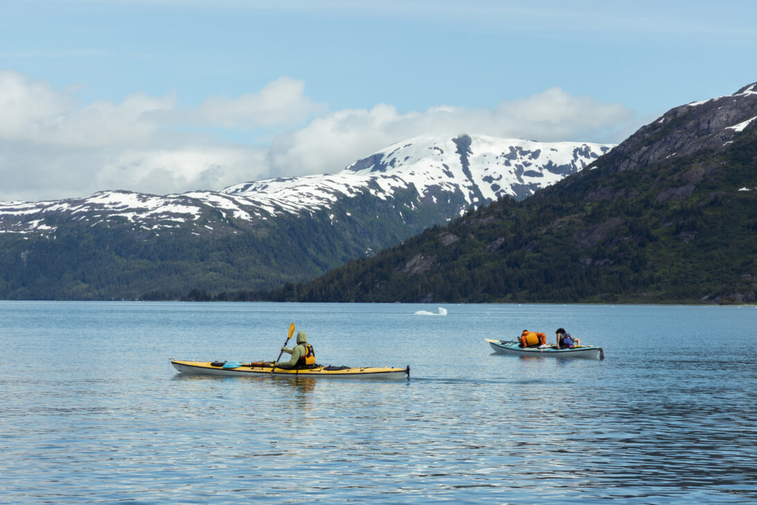 two sea kayaks in the ocean in front of snowy Alaska mountains