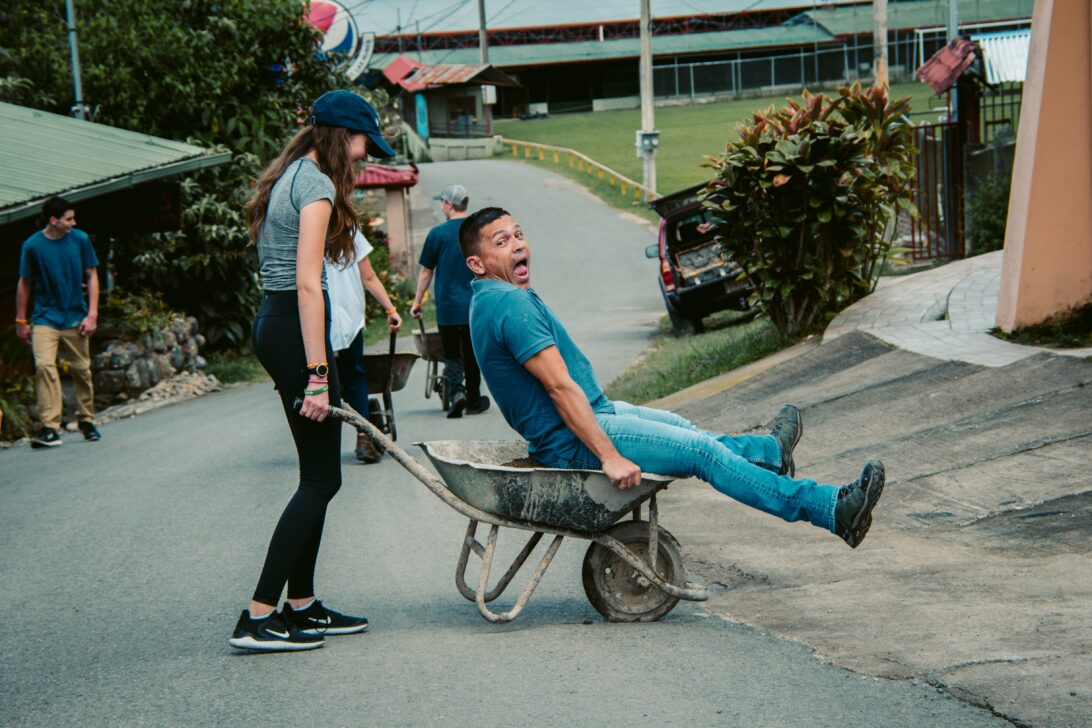 student pushing a wheel chair with a man in it laughing