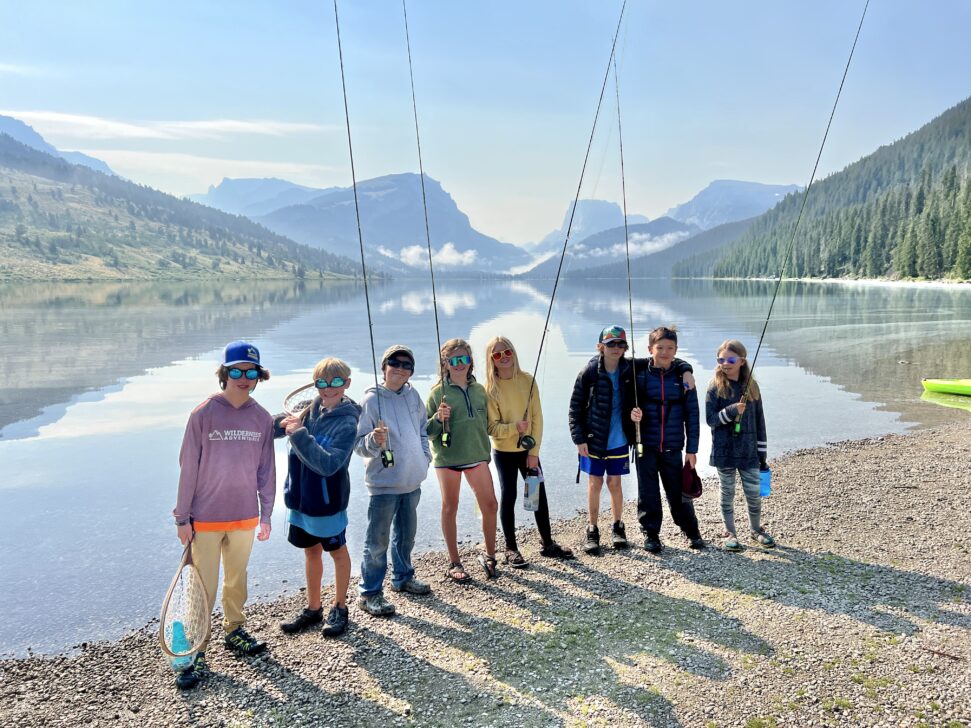 students posing with their fly fishing rods in front of a lake