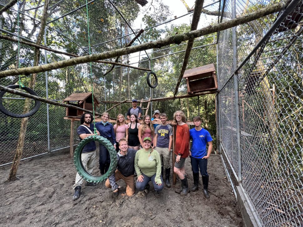 group posing with the monkey enclosure at a sanctuary they helped build