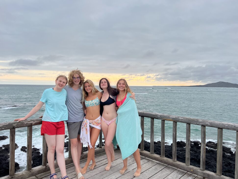 students in swimming suits and towels posing on a deck in front of the ocean