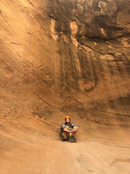 Camper wearing a helmet sits on a orange rock in a canyon