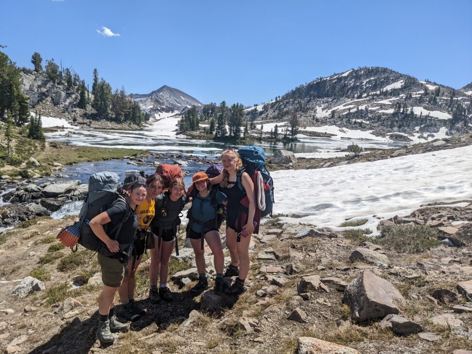 students backpacking and posing in front of a snowy alpine lake