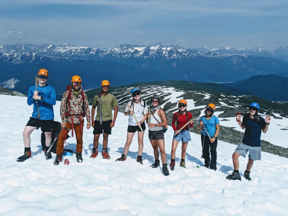 A group stands on a patch of snow with ice climbing gear