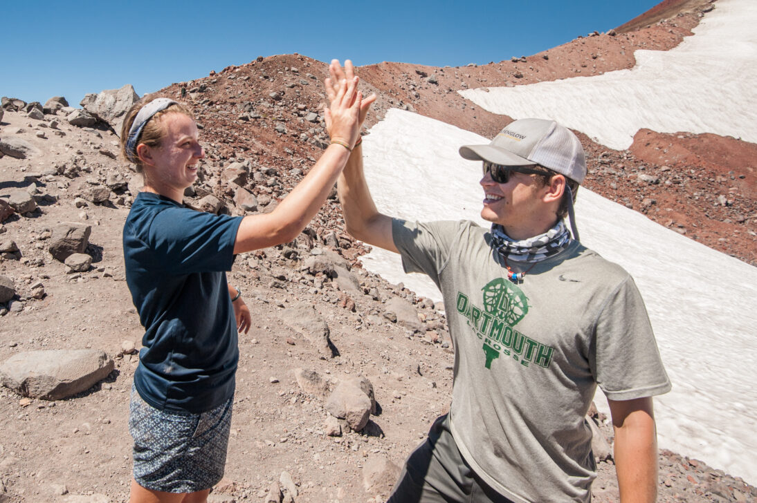 two students high fiving at the top of a rocky mountain