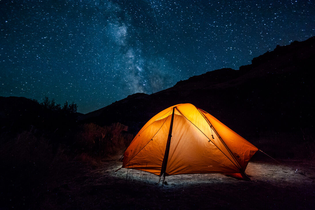 night time picture of an illuminated orange tent with the milky way in the sky