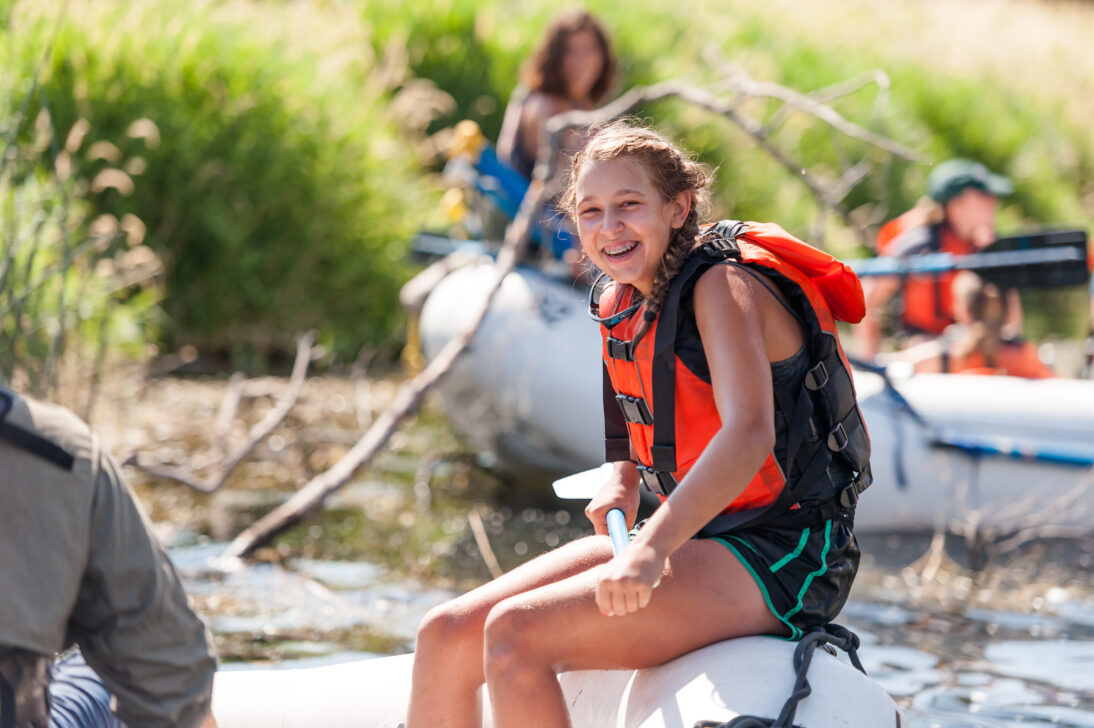 student laughing on the edge of a rafting boat in her life jacket
