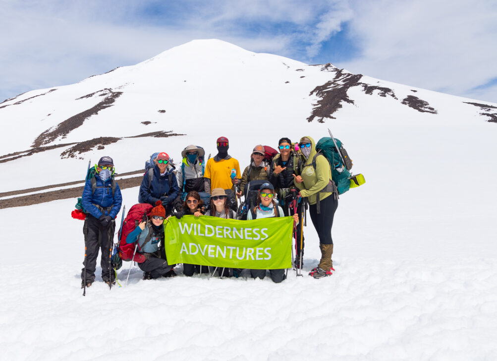 Wilderness Adventures Group Holding banner near the snow capped summit of a mountain