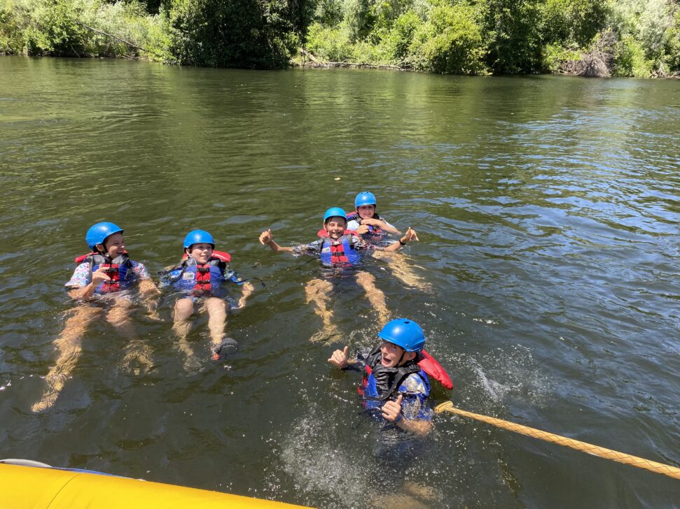 5 students floating in a river with helmets and PFDs after jumping out of a whitewater raft