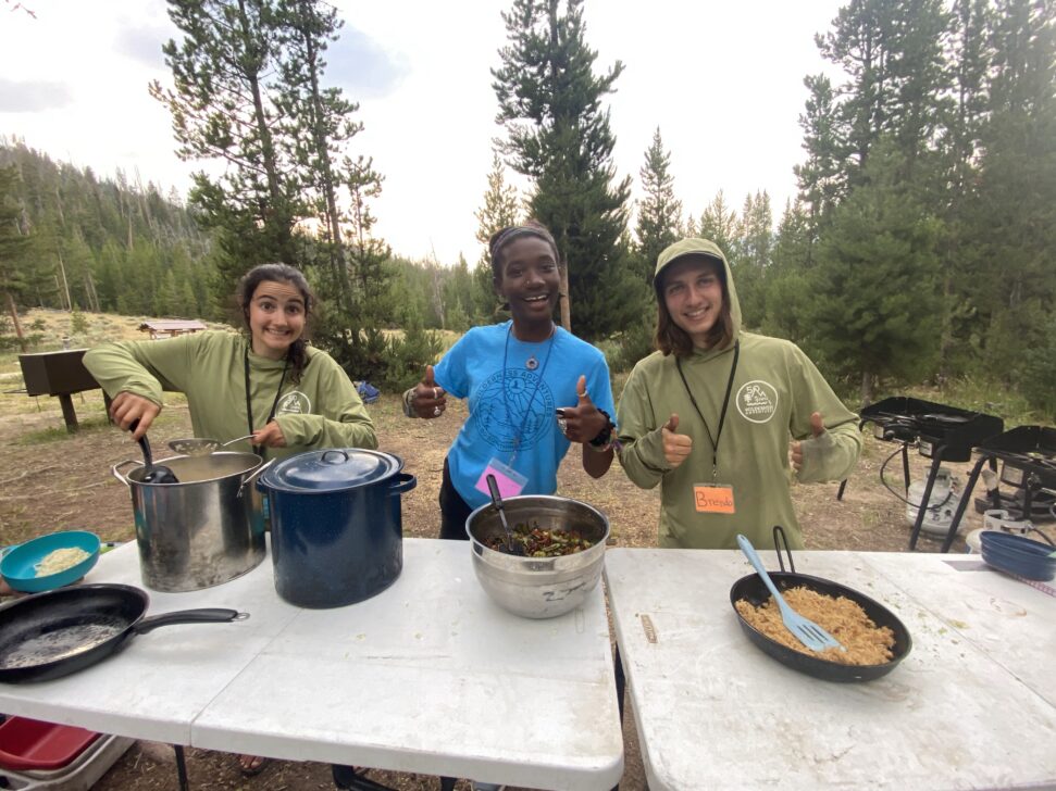 Three people preparing camping food