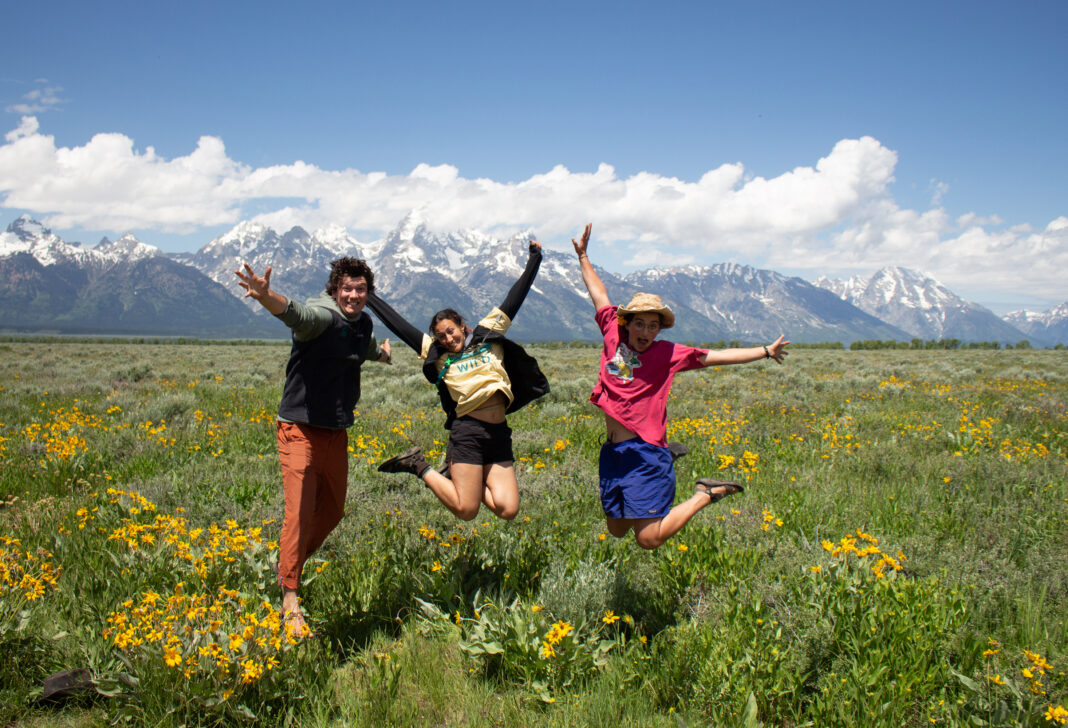 Three people jumping in the air in front of the Tetons.