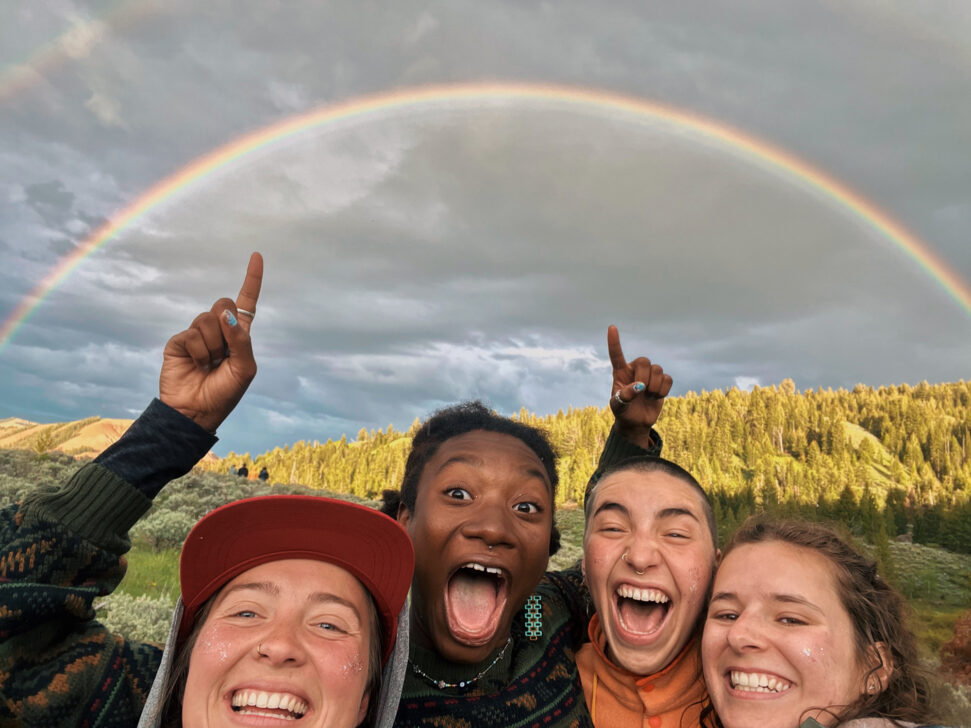 Four people underneath a big rainbow smiling.