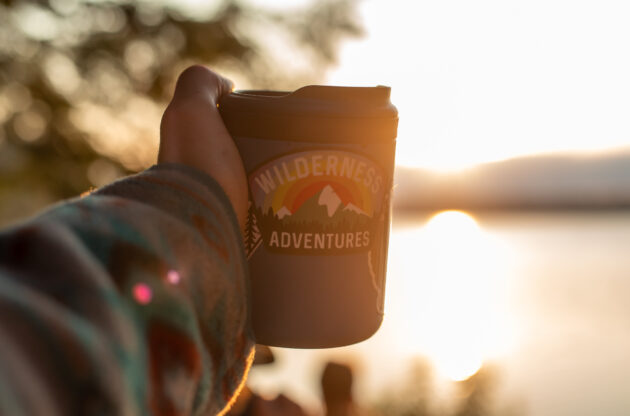 travel mug with a Wilderness Adventures sticker on it in front of the sunset