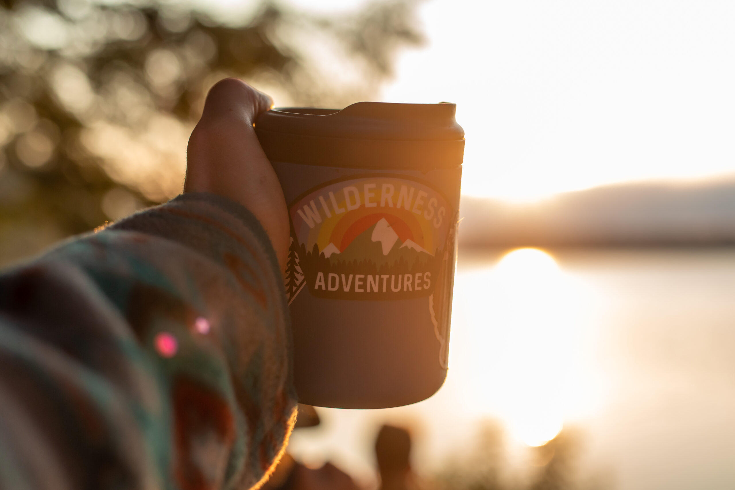 travel mug with a Wilderness Adventures sticker on it in front of the sunset