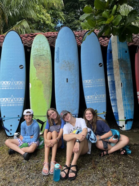 4 girls sit in front of surfboards leaning against the wall