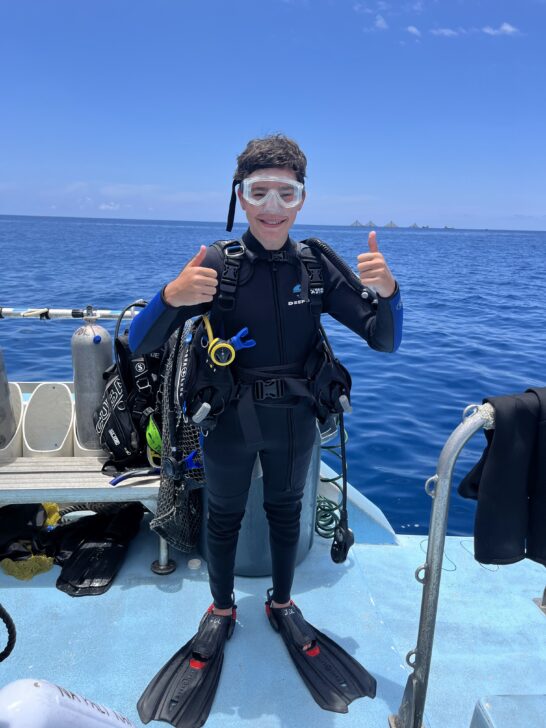 student giving 2 thumbs up on a boat in scuba diving gear