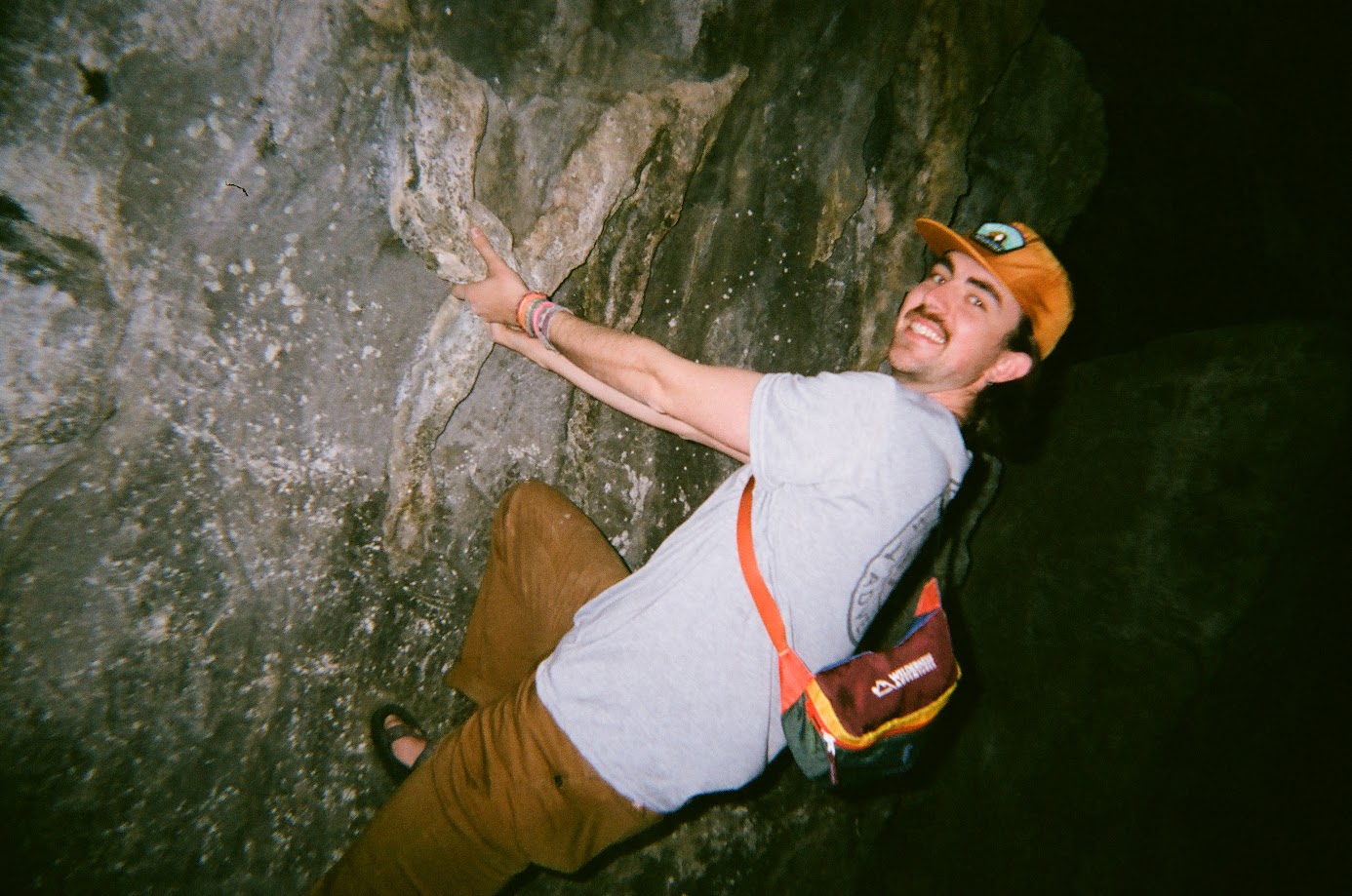 Man rock climbing in a cave smiling at the camera.