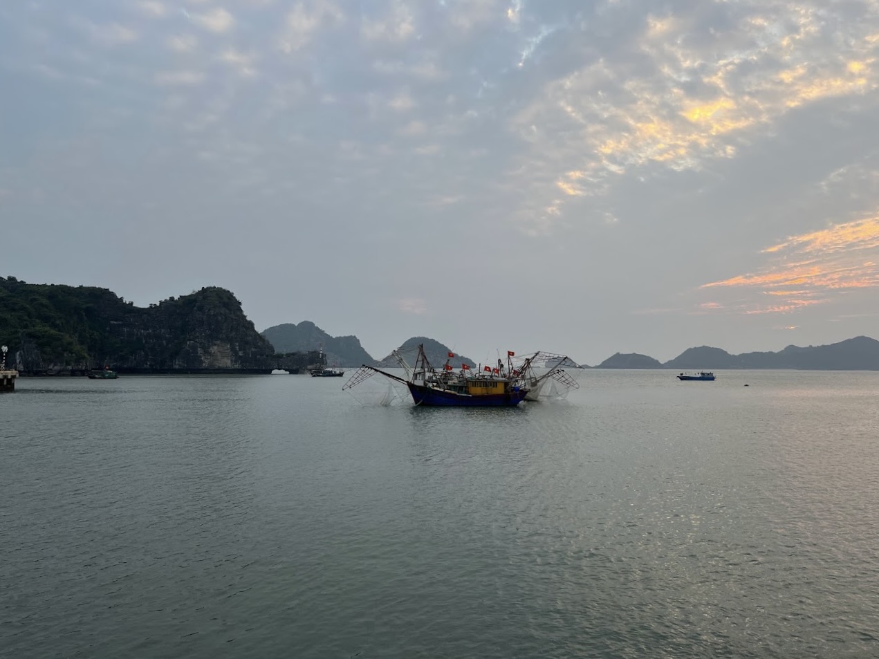 Cloudy sunset over the ocean and rocky coast of Vietnam. Oldschool fishing boat in the center of the image with many flags and nets.