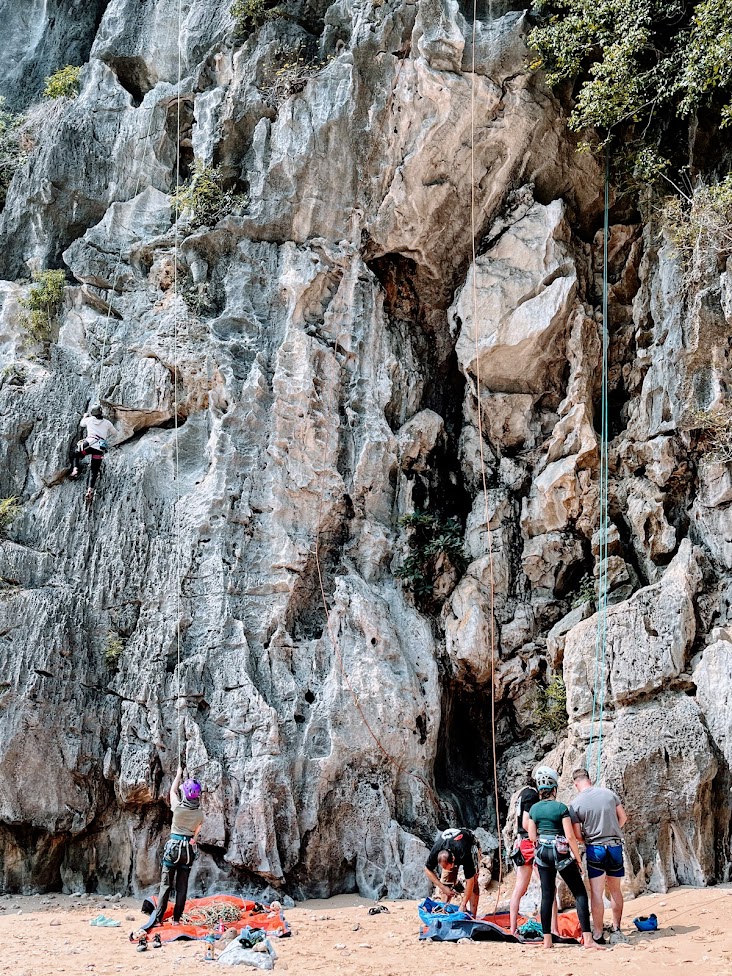 Group of rock climbers at the base of a limestone wall belaying a climber and gathering gear. 