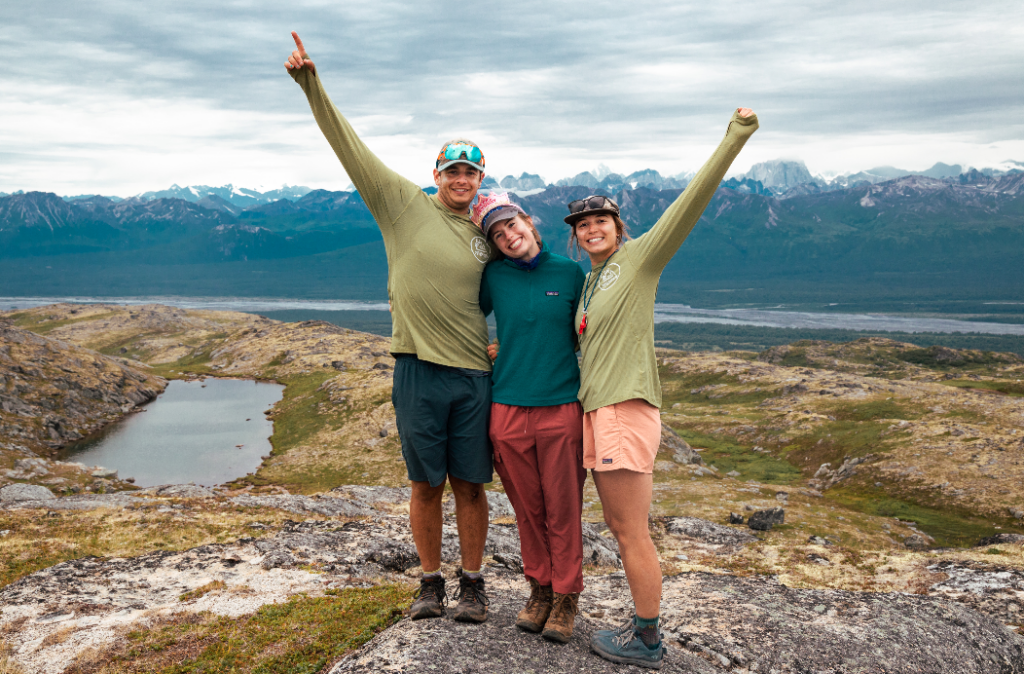 Three people smiling in the mountains.