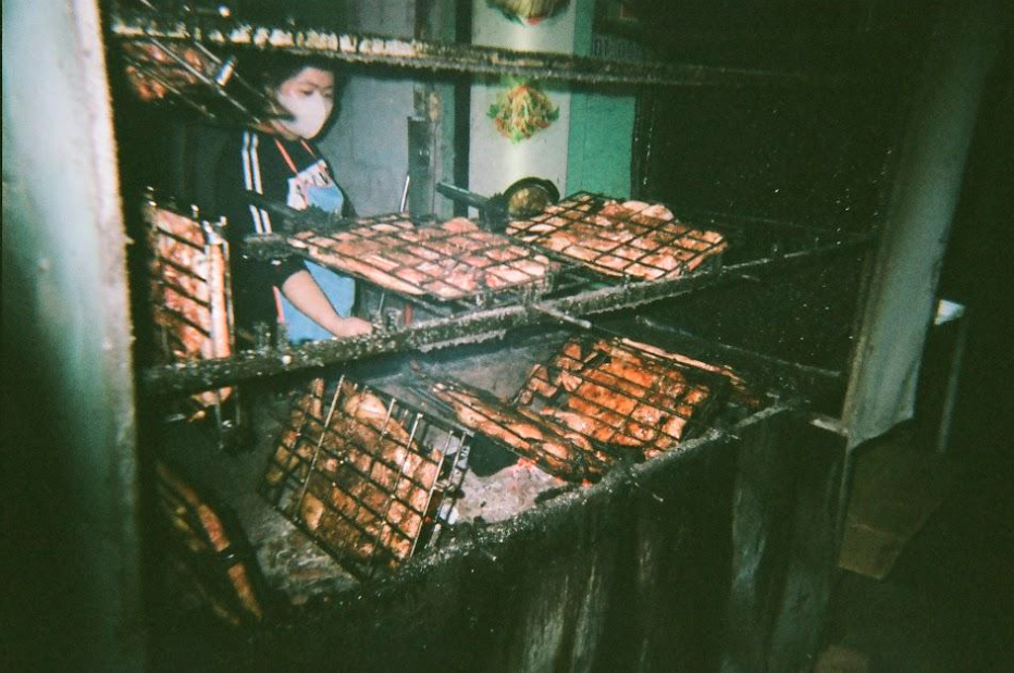 Vietnamese woman cooking chicken strips over embers.
