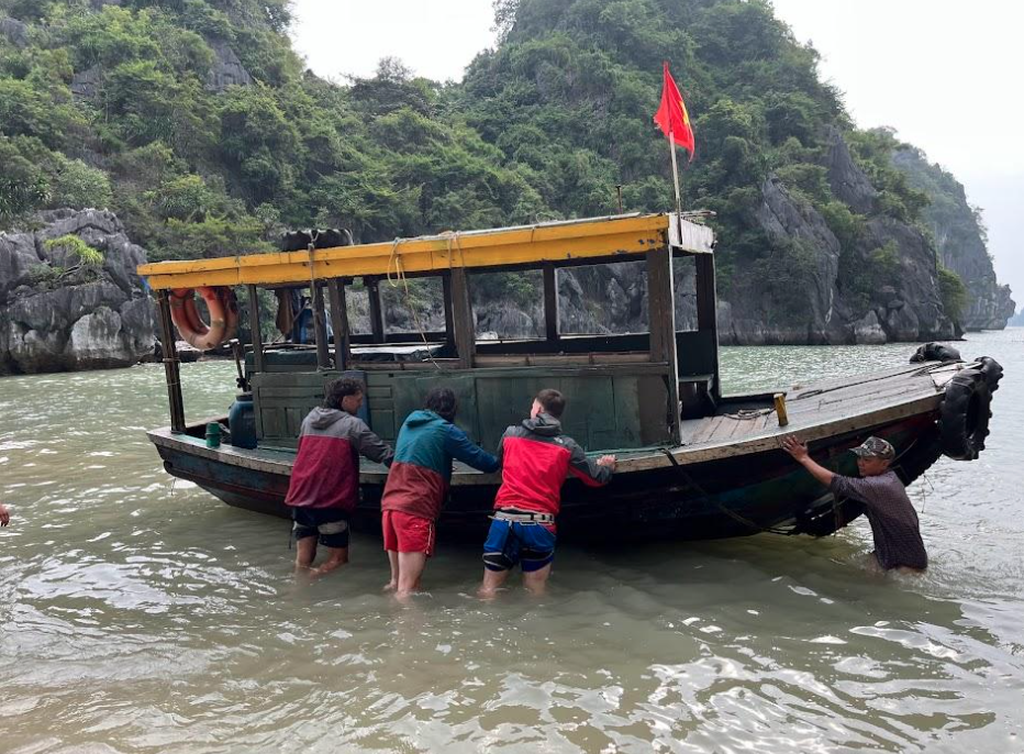 Four people pushing a boat off the shore of a rocky coast in Vietnam.