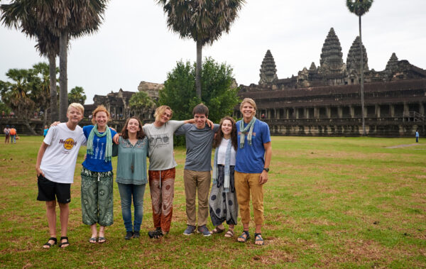 Group of travelers smiling with their arms around each other in front of ancient temple.