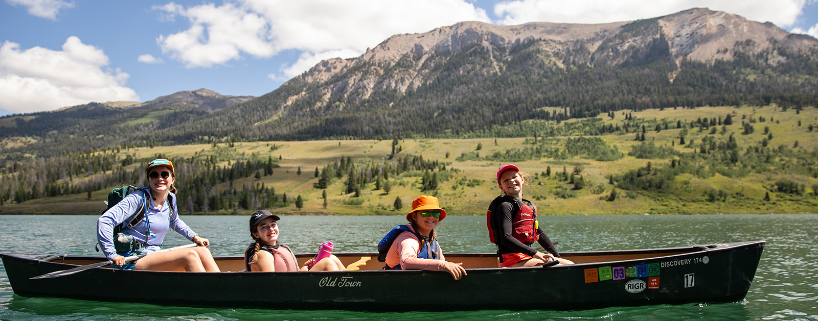 Four campers paddling in a canoe on a lake.