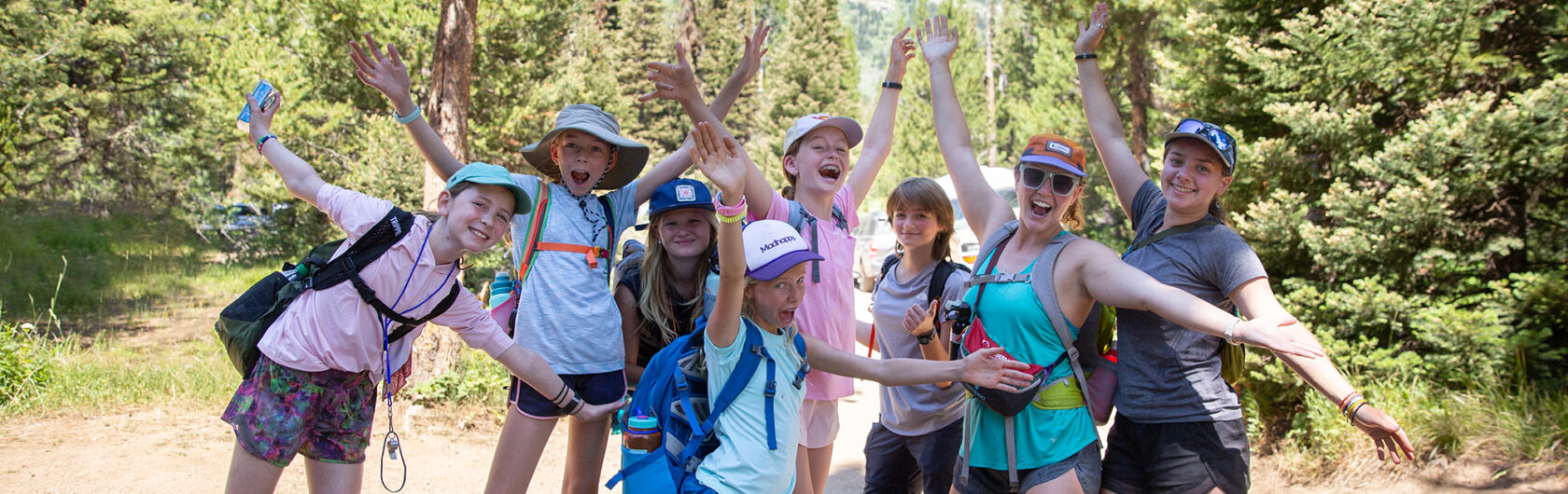 Group of girls with their hands in the air and big smiles on a hike.