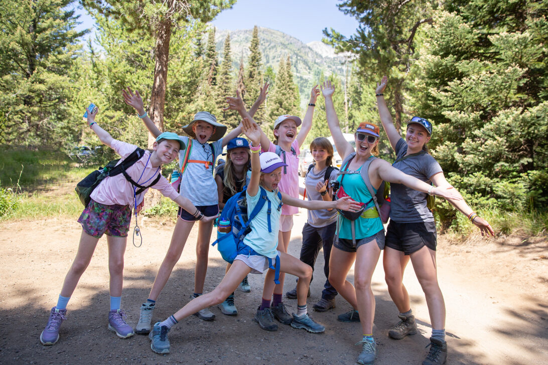 Group of girls with their hands in the air and big smiles on a hike.