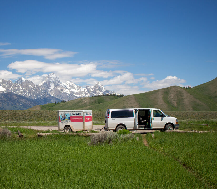 15 passenger Ford van with a uHaul trailer attached in front of the Tetons.